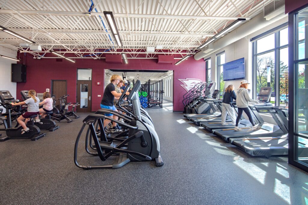Fitness room with students on the cardio machines and the garage door open to the weight room