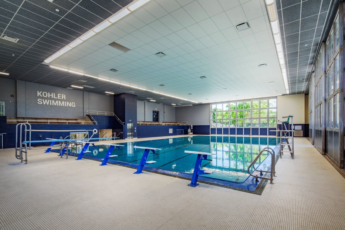 Indoor pool looking at bleachers with signage and pool entry